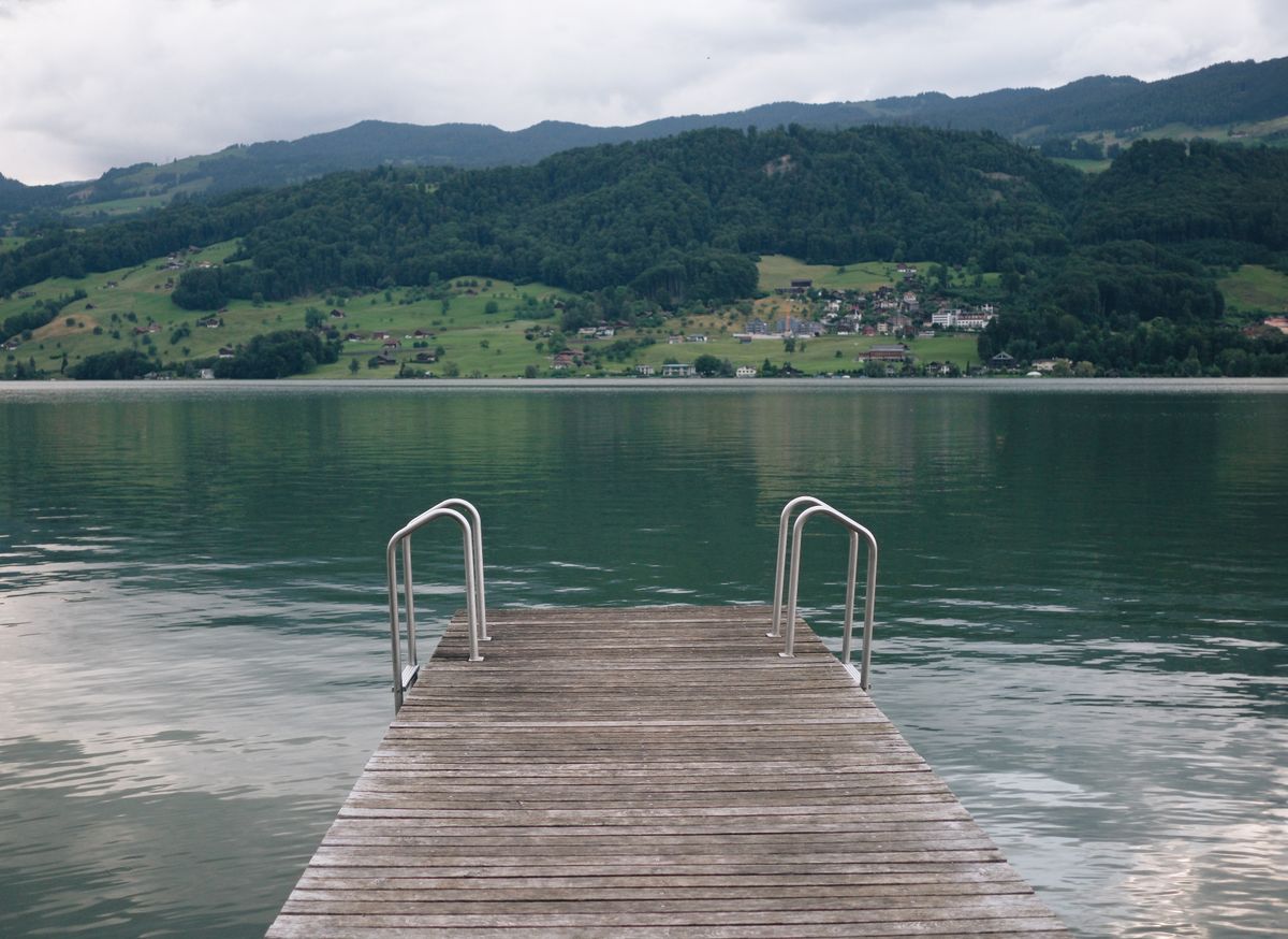 Ruhiger Alpensee mit Badesteg, Blick auf ein Dorf am gegenüberliegenden Ufer